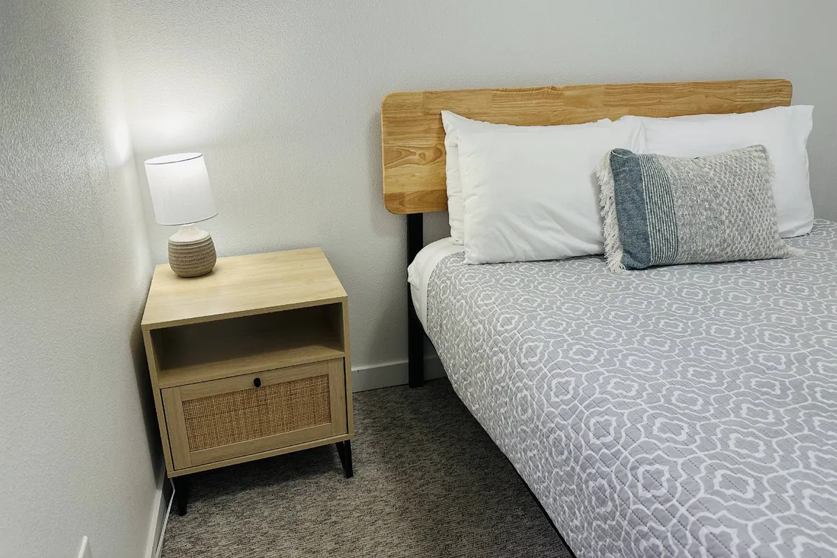 A relaxed and cozy bedroom environment, featuring a bed with a decorative pillow, a nightstand, and a lamp. The soft lighting and intimate atmosphere suggest a space designed for restful nights and refreshing mornings.